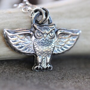 May include: A silver owl pendant with detailed wings and a textured surface. The owl has large, round eyes and a beak.