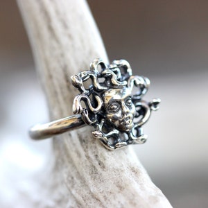 Puede incluir: Un anillo de plata con un dise&ntilde;o detallado de la cabeza de Medusa con serpientes como cabello.