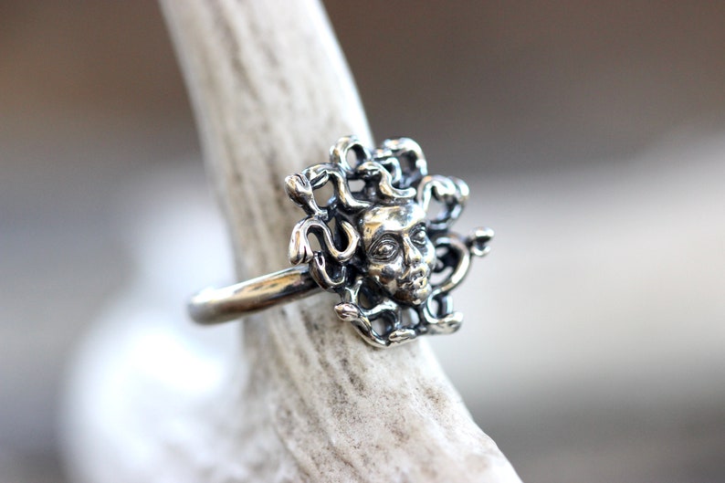 Puede incluir: Un anillo de plata con un dise&ntilde;o detallado de la cabeza de Medusa con serpientes como cabello.