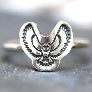 May include: A silver ring with an owl design. The owl is depicted with its wings spread out and its head facing forward. The ring is made of sterling silver and has a polished finish.