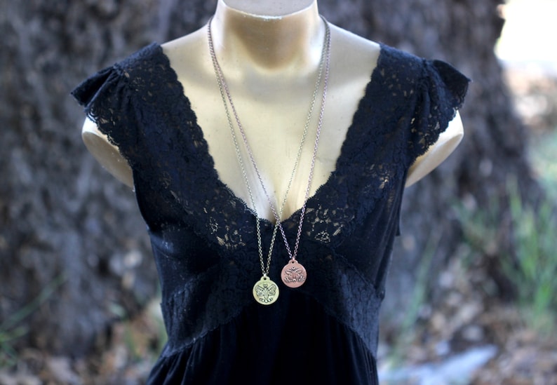 May include: Two silver chains with a round pendant on each. The pendants are both detailed with a floral design. One pendant is gold and the other is copper.