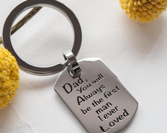 Puede incluir: Llavero plateado con un colgante de chapa de perro. La chapa está grabada con las palabras "Dad, You will Always be the first man I ever Loved". El llavero se muestra con acentos florales amarillos.