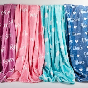 May include: A collection of soft blankets in shades of pink, purple, turquoise, and blue. Each blanket features a repeating pattern of names and hearts in white script. The blankets are made of a plush material, perfect for snuggling.