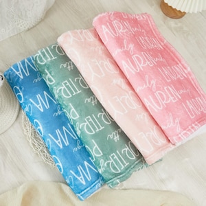 Può includere: Quattro coperte in peluche nei toni del blu, verde, rosa e rosa. Ogni coperta è stampata con un nome bianco in un carattere a script. Le coperte sono piegate e disposte fianco a fianco, mostrando la morbida consistenza e il design personalizzato.
