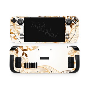 Op de afbeelding: Een witte Steam Deck skin met een bruin en goudkleurig bloemenpatroon. De skin bedekt de voor- en achterkant van het apparaat, met de tekst "Stick It And Play" zichtbaar op het scherm.