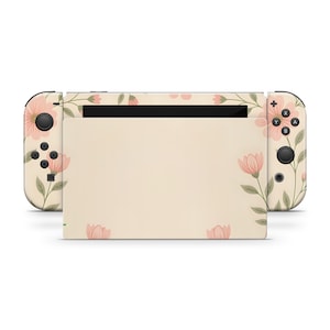 Op de afbeelding: Een crèmekleurige Nintendo Switch-console met een bloemenontwerp. Het ontwerp heeft roze bloemen en groene bladeren. De knoppen en joysticks van de console zijn zwart.