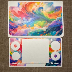 Puede incluir: Juego de dos pegatinas para consola de juegos, con un diseño abstracto y colorido. La pieza superior es rectangular con una parte superior curvada, y la pieza inferior es rectangular con recortes circulares y un rectángulo blanco central.