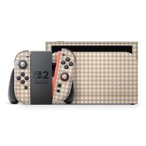 Könnte beinhalten: Eine Nintendo Switch-Konsole und Controller mit einem beige-weißen Vichy-Muster. Die Controller haben schwarze Knöpfe und blaue und rote Akzente. Die Switch-Dockingstation weist ebenfalls das gleiche Vichy-Design auf.