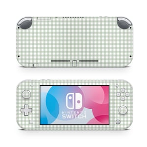 Peut inclure: Une console Nintendo Switch Lite avec un motif vichy vert clair et blanc. L'écran affiche le logo Nintendo Switch sur un fond rose et bleu. La console a des boutons de commande gris.