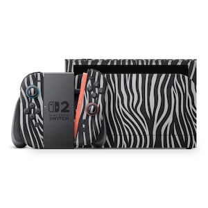 Puede incluir: Una consola Nintendo Switch y mandos Joy-Con con un diseño de rayas de cebra en blanco y negro. Los mandos tienen detalles en color turquesa y rojo. La consola está en su estación de acoplamiento.