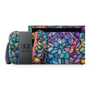Peut inclure: Une console Nintendo Switch et des manettes avec un motif de vitrail. Les manettes sont noires et corail, et la console a un centre gris. Le motif présente une mosaïque de formes bleues, violettes et jaunes.