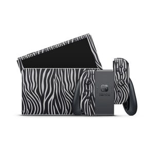 Puede incluir: Una consola Nintendo Switch y accesorios con un diseño de rayas de cebra en blanco y negro. El conjunto incluye la consola, los mandos Joy-Con y una base de carga. El diseño cubre la consola y los mandos.
