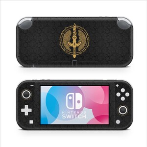 Peut inclure: Une console de jeu portable noire avec un emblème d'épée dorée entouré d'un motif circulaire au dos. La face avant présente un écran avec le logo Nintendo Switch, une croix directionnelle, des boutons d'action et deux joysticks sur un boîtier noir.