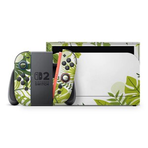 Peut inclure: Une console Nintendo Switch et ses manettes avec un motif de feuilles tropicales blanches et vertes. Les manettes sont noires, vertes et corail. La console porte l'inscription "Nintendo Switch".