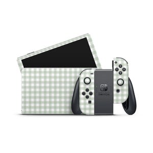 Puede incluir: Una consola Nintendo Switch y mandos con un patrón de cuadros vichy verde claro y blanco. La consola está en una estación de acoplamiento y los mandos Joy-Con están conectados. La pantalla de la Switch es negra.