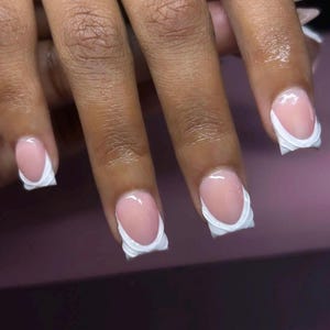 May include: Close-up of four fingernails with a white, scalloped French manicure design. The nails are short and oval-shaped.