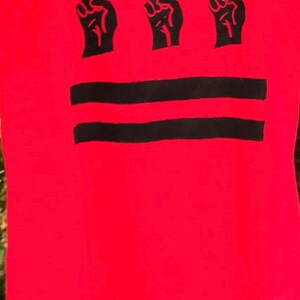 May include: Red t-shirt with three black raised fists and two black horizontal stripes.