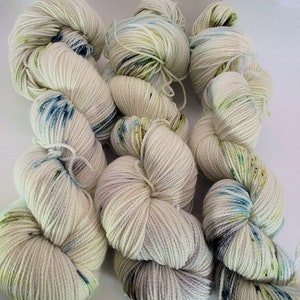 Op de afbeelding: Klossen wit garen met vlekken van blauw, groen en grijs.