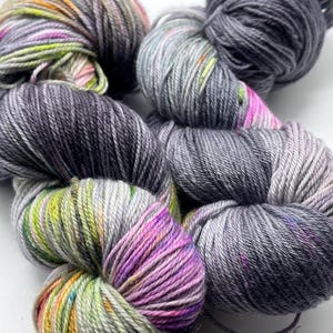 May include: Two skeins of yarn, one is a variegated grey with pink and green flecks, the other is a solid grey.