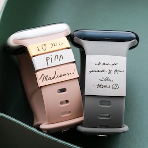 May include: Two silicone watch bands with metal charms. The pink band features three charms engraved with "I heart you", "Finn", and "Madison". The gray band features a single wide metal charm engraved with "I am so proud of you Love, mom" and a smiley face.