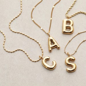 May include: Four gold necklaces with chunky letter pendants. The letters are A, B, C, and S.