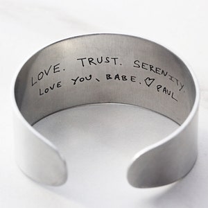 May include: Silver cuff bracelet with an engraved message that reads "Love. Trust. Serenity. Love you, babe. ♥ Paul."