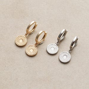 May include: Two pairs of earrings with a circular design. One pair is gold with a sun-like design and the other pair is silver with a similar design.