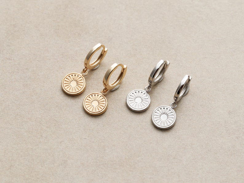 May include: Two pairs of earrings with a circular design. One pair is gold with a sun-like design and the other pair is silver with a similar design.