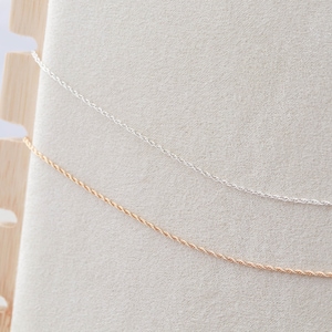 May include: Two delicate chains, one silver and one gold, are displayed on a white background. The chains are both twisted rope style.