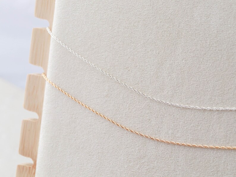 May include: Two delicate chains, one silver and one gold, are displayed on a white background. The chains are both twisted rope style.