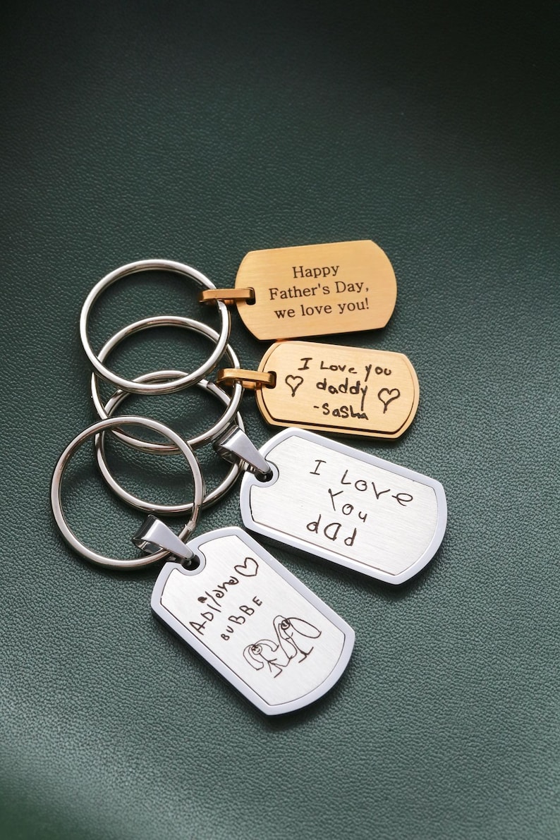 May include: Four metal dog tag keychains with silver and gold finishes. Two gold tags feature engraved text: "Happy Father's Day, we love you!" and "I love you daddy -Sasha". Two silver tags feature engraved handwriting and a drawing of two figures.