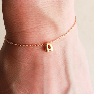 May include: A gold chain bracelet with a single letter 'A' charm. The charm is a simple, rounded letter.