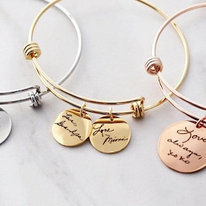 a collection of personalized bracelet charms, each with a handwritten message engraved on it. The charms are arranged in a row, showcasing the variety of messages and designs.