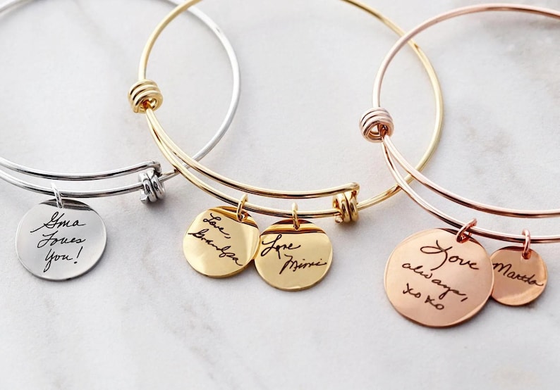a collection of personalized bracelet charms, each with a handwritten message engraved on it. The charms are arranged in a row, showcasing the variety of messages and designs.