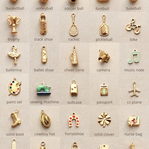 May include: A collection of gold-toned charms in various shapes, including sports equipment like a basketball and a soccer ball, along with other items such as a camera, a sewing machine, and a nurse bag. Each charm has a small loop for attaching to a bracelet or necklace.