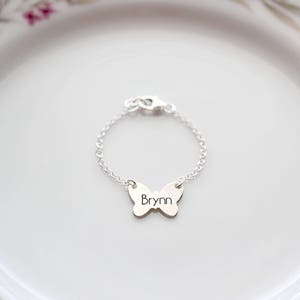 Pode incluir: Um bracelete de prata com um fecho de borboleta com o nome "Bryn" gravado.