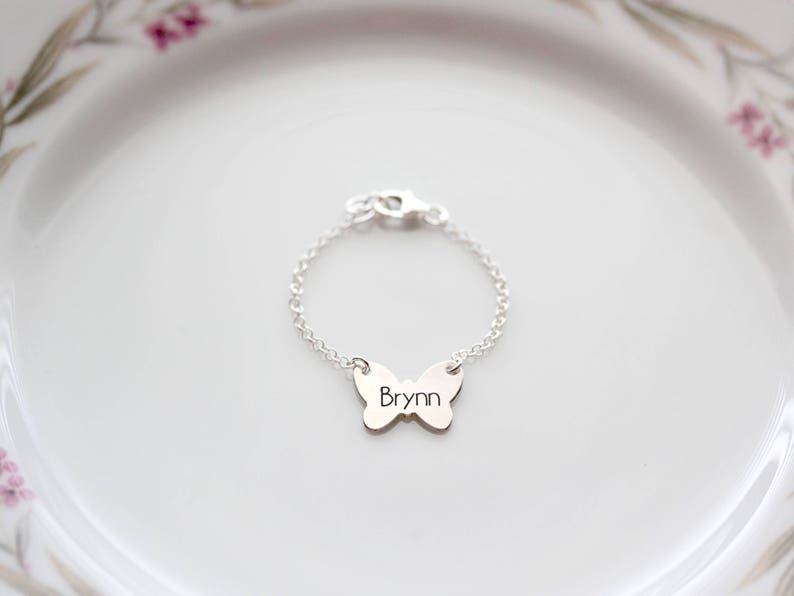 Pode incluir: Um bracelete de prata com um fecho de borboleta com o nome "Bryn" gravado.