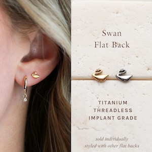 May include: Gold swan stud earrings and a gold hoop earring with a dangling diamond. The image also shows a silver swan earring. The text on the image says "Swan Flat Back" and "TITANIUM THREADLESS IMPLANT GRADE".