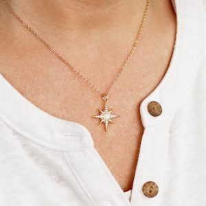 May include: A gold chain necklace with a starburst pendant featuring a white stone in the center and smaller stones around the edges.