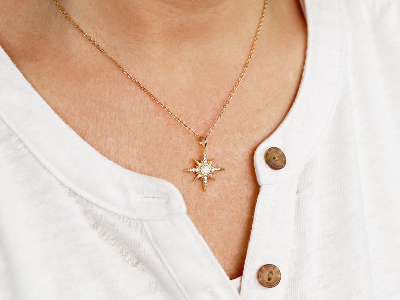 May include: A gold chain necklace with a starburst pendant featuring a white stone in the center and smaller stones around the edges.