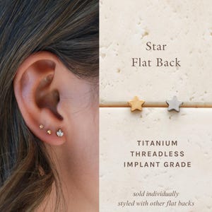 May include: A titanium threadless implant grade flat back earring featuring a star shape. The image displays a gold-toned star stud and a silver-toned star stud, with text reading Star Flat Back, Titanium Threadless Implant Grade.