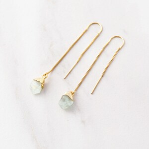 May include: A pair of gold dangle earrings with light blue crystal stones. The earrings have a delicate chain design.