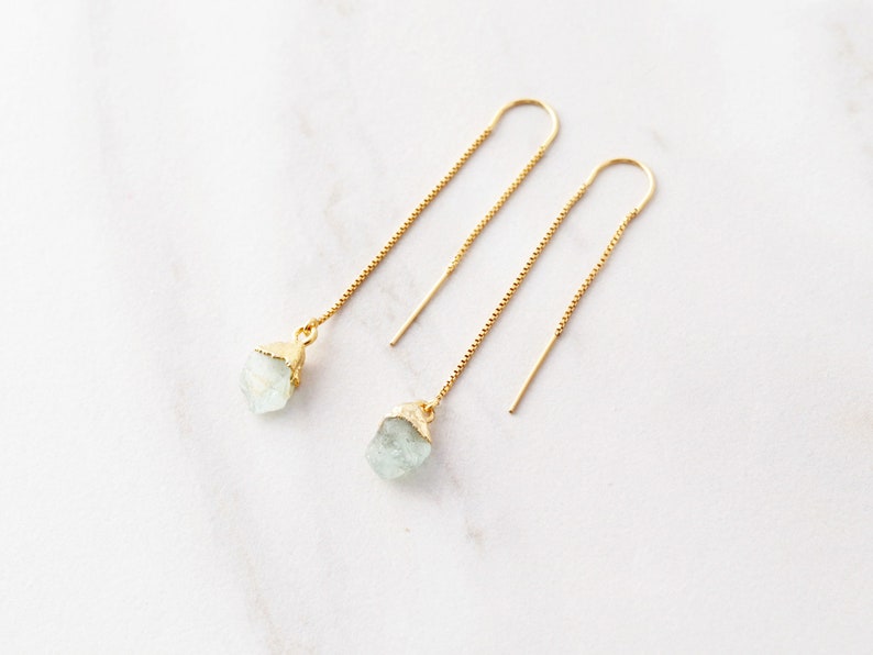 May include: A pair of gold dangle earrings with light blue crystal stones. The earrings have a delicate chain design.