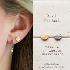 May include: Gold shell-shaped stud earrings and a gold hoop earring with a small charm are shown on an ear. The image also displays two shell-shaped flat back earrings, one gold and one silver, with the text "Shell Flat Back".
