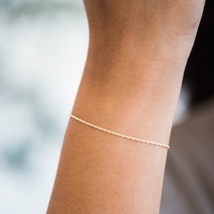 May include: A delicate gold chain bracelet with a twisted rope design.