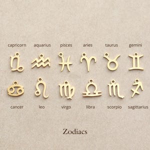 May include: Gold-colored zodiac charms, each with a unique symbol, are displayed against a neutral background. The word "Zodiacs" is printed below the charms. The charms include symbols for Capricorn, Aquarius, Pisces, Aries, Taurus, Gemini, Cancer, Leo, Virgo, Libra, Scorpio, and Sagittarius.