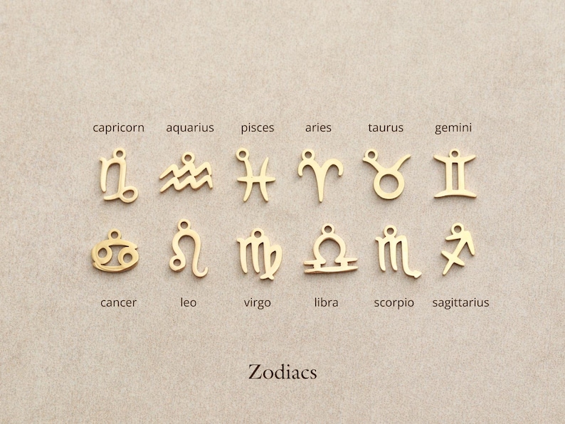 May include: Gold-colored zodiac charms, each with a unique symbol, are displayed against a neutral background. The word "Zodiacs" is printed below the charms. The charms include symbols for Capricorn, Aquarius, Pisces, Aries, Taurus, Gemini, Cancer, Leo, Virgo, Libra, Scorpio, and Sagittarius.