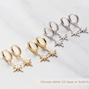 May include: A set of six gold and silver hoop earrings with a dangling star charm. Each star charm has a white opal center and is surrounded by smaller clear stones. The text "Choose either CZ base or Solid base" is visible at the bottom of the image.