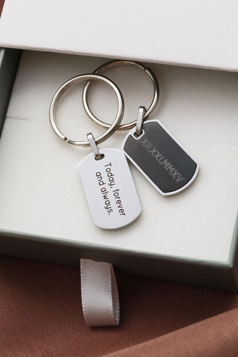 May include: Two metal keychains with rectangular tags attached to silver split rings. One tag is silver with the engraved text Today, forever and always. The other tag is dark gray with the engraved Roman numeral date XII.XXI.MMXV.