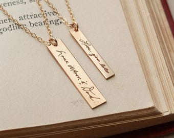 May include: Two gold-toned bar necklaces with delicate chains. The longer bar is engraved with the cursive text Love Mom & Dad, while the shorter bar features the cursive inscription Love you lots. Both pendants hang from thin, matching gold-toned chains.